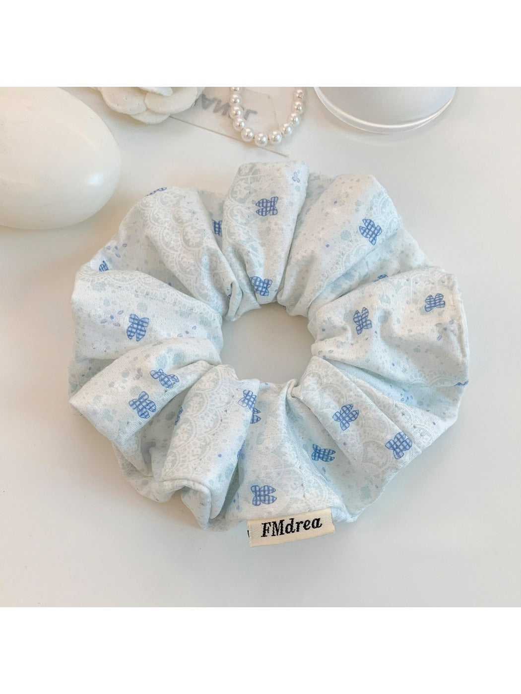 Blue fabric scrunchie with white bow design shown from side angle