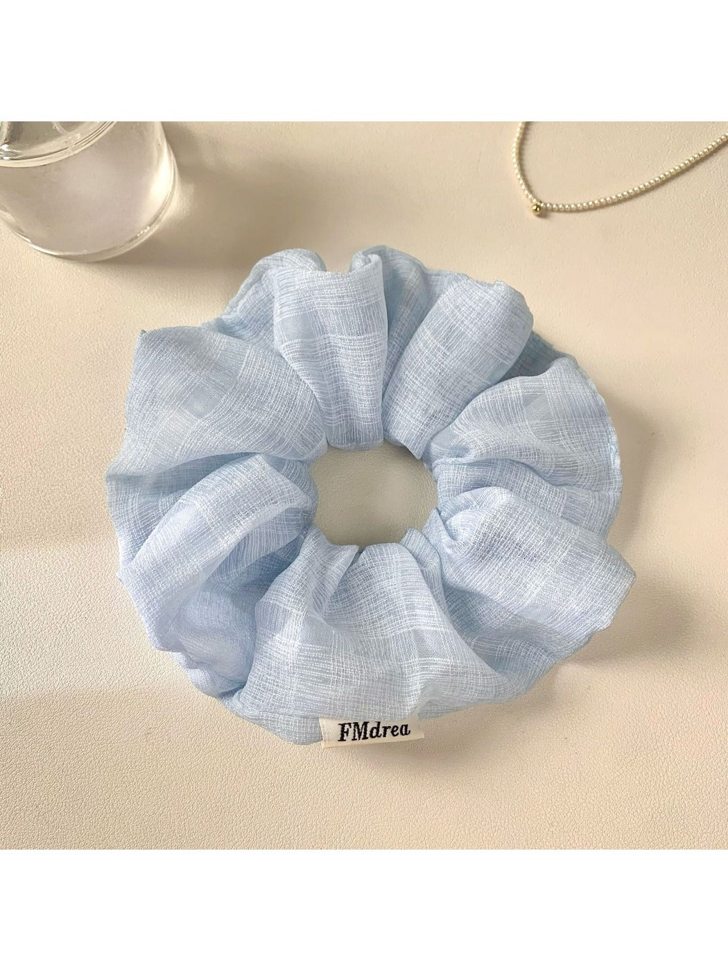 Multiple solid color ruched scrunchies arranged in a row on a neutral background