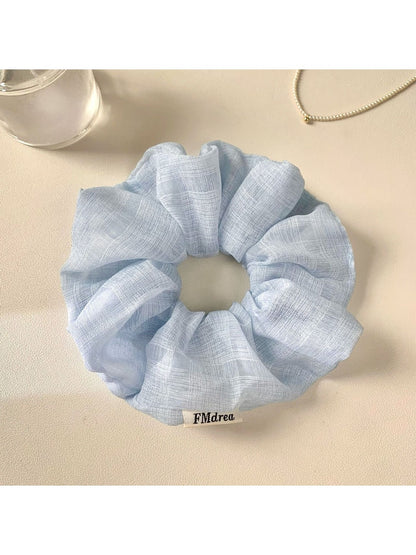 Multiple solid color ruched scrunchies arranged in a row on a neutral background