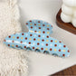 Blue hair claw clip with white polka dots resting on a wooden surface