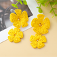 Earedge raffia drop earrings with floral pendant shown against a green leaf background