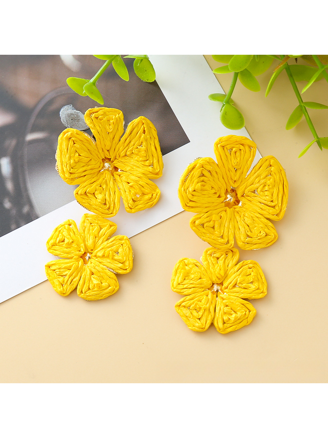 Earedge raffia drop earrings with floral pendant shown against a green leaf background