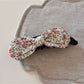 Beau bow hair clip held in hand, showing clip mechanism and painted fabric detail