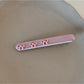 Pink bow hair clip held between fingers showing size and texture