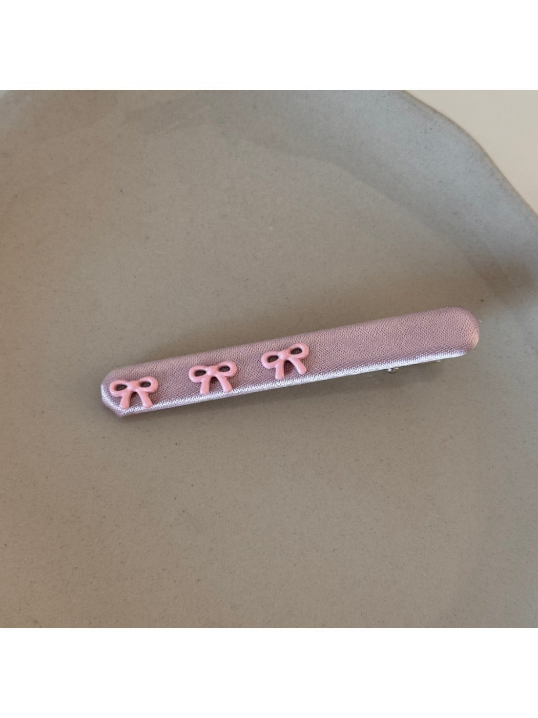 Pink bow hair clip held between fingers showing size and texture
