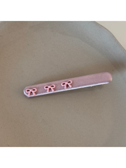 Pink bow hair clip held between fingers showing size and texture