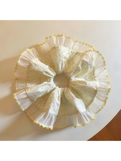 Yellow floral scrunchie held in hand highlighting pleated design