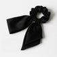 Satin bow hair tie in soft pink color placed next to matching satin ribbon