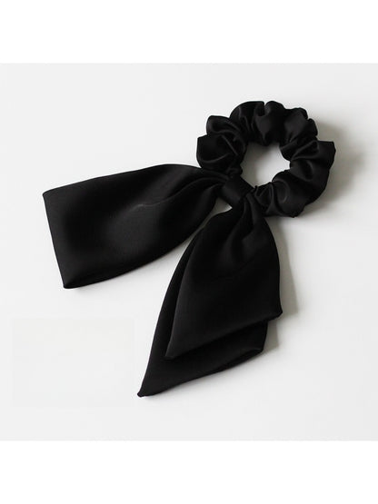 Satin bow hair tie in soft pink color placed next to matching satin ribbon