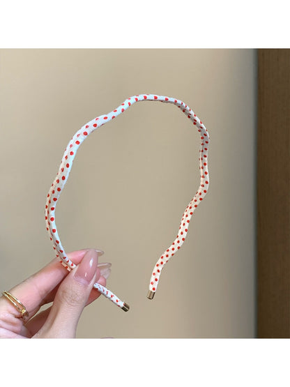 Side view of thin wavy headband with black polka dots on white background