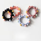 Close-up of colorful beaded hair ties arranged in a circle on a white background