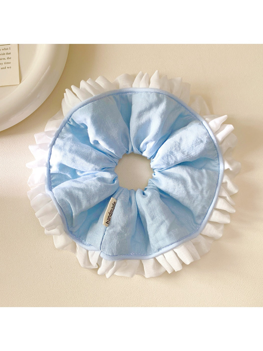White scrunchie with blue ruffle detail on a plain background
