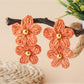 Pair of raffia flower shaped earrings placed on textured fabric surface