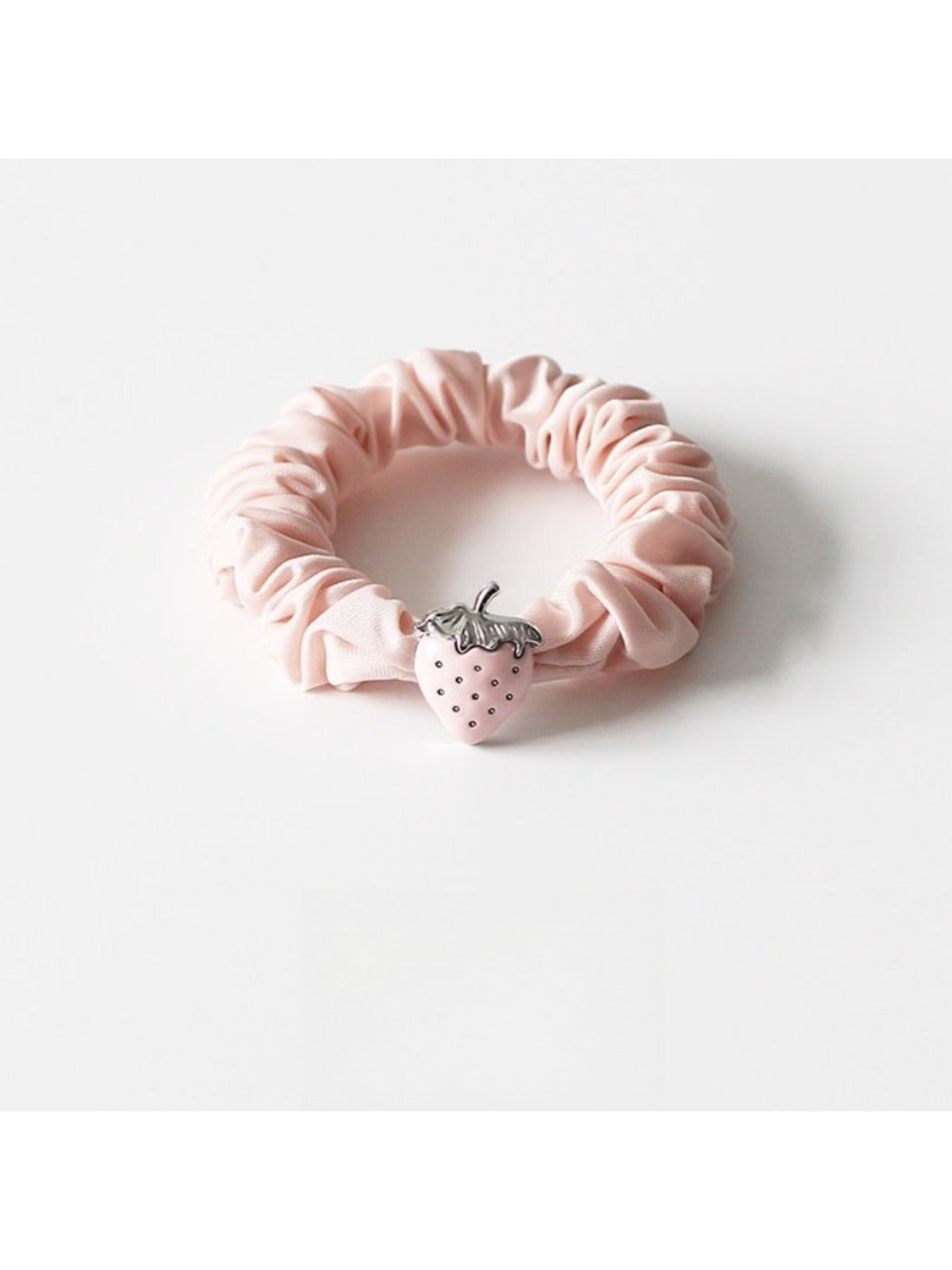 Strawberry hair tie placed next to fresh strawberries for size comparison