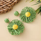 Pair of raffia sunflower earrings placed on a natural woven fabric