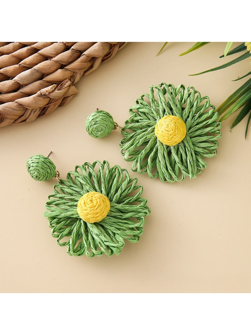 Pair of raffia sunflower earrings placed on a natural woven fabric