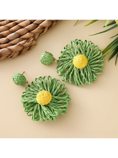 Pair of raffia sunflower earrings placed on a natural woven fabric