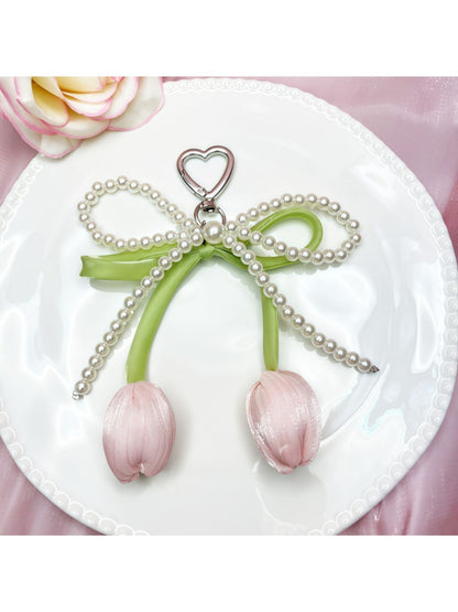 Minimalist bow and tulip pendant keychain displayed on a wooden surface