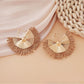 Earedge raffia woven fan shape earrings hanging against natural wood background