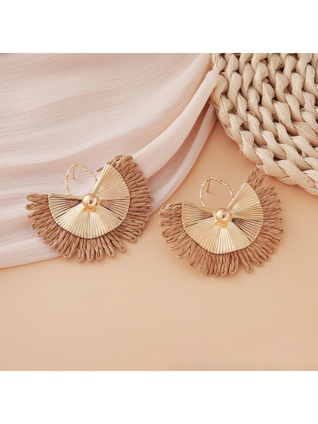 Earedge raffia woven fan shape earrings hanging against natural wood background