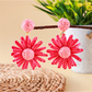 Bohemian style daisy floral raffia earrings placed next to green leaves