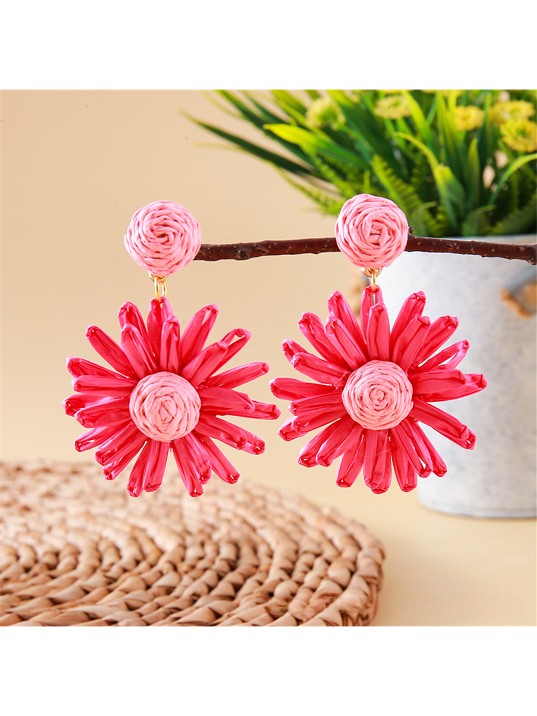 Bohemian style daisy floral raffia earrings placed next to green leaves