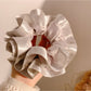 Gifty satin ruffle scrunchie in cream color placed on a marble surface