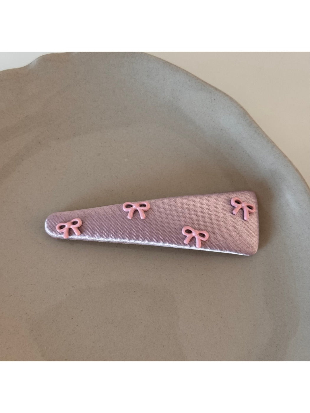 Pink bow hair clip displayed on a flat surface with a shadow