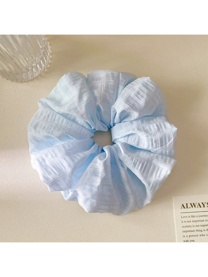 Gifty scrunchie placed on a white surface, showcasing its bright multicolor checkered pattern