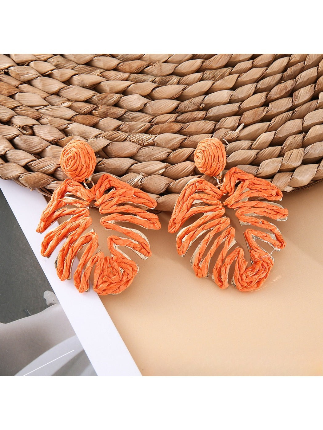 Close-up of raffia woven hollow leaf shaped earrings highlighting woven details