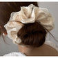 Beige satin scrunchie displayed on a wooden surface