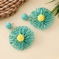 Raffia sunflower earrings displayed with green leaves for a natural look