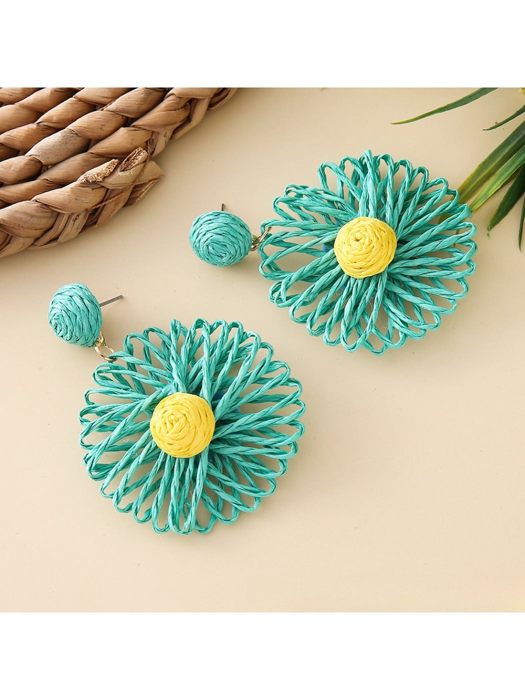 Raffia sunflower earrings displayed with green leaves for a natural look
