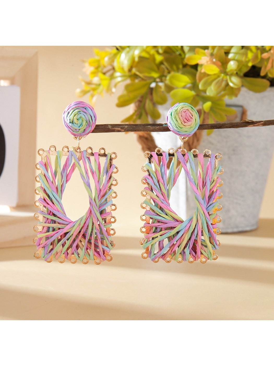 Pair of Earedge raffia wrapped square earrings hanging on a jewelry stand