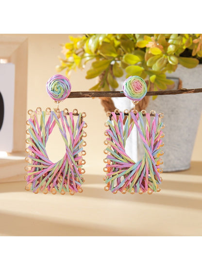 Pair of Earedge raffia wrapped square earrings hanging on a jewelry stand