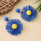 Raffia sunflower earrings hanging on a wooden display stand