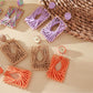 Earedge square earrings with raffia wrapping displayed on a wooden surface