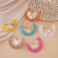 Earedge raffia woven fan shape earrings displayed hanging on a stand