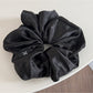 Glossy satin scrunchie in pink coiled loosely on a white surface