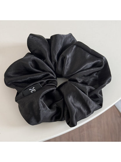 Glossy satin scrunchie in pink coiled loosely on a white surface