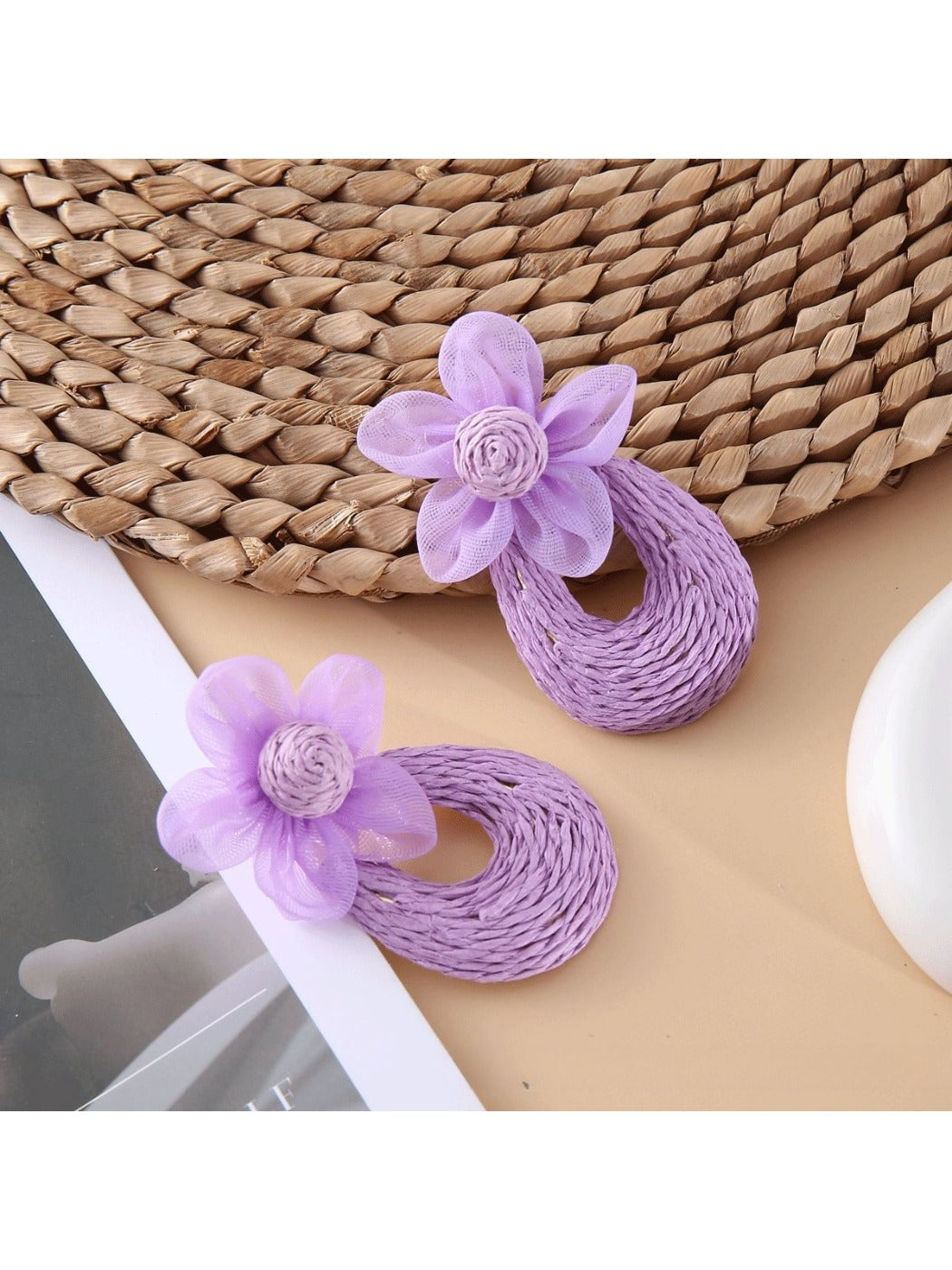 Sweet Raffia Flower Shaped Stud Earrings displayed with green leaves background