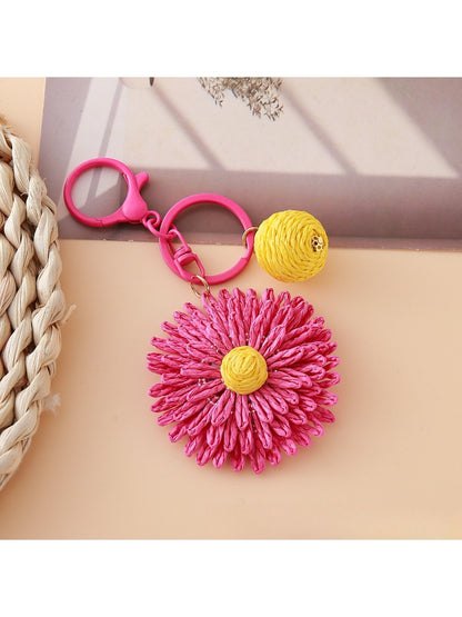 Hand holding the raffia woven sunflower keychain against a plain background