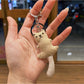 Bear keychain with a smiling expression and long tail curled around