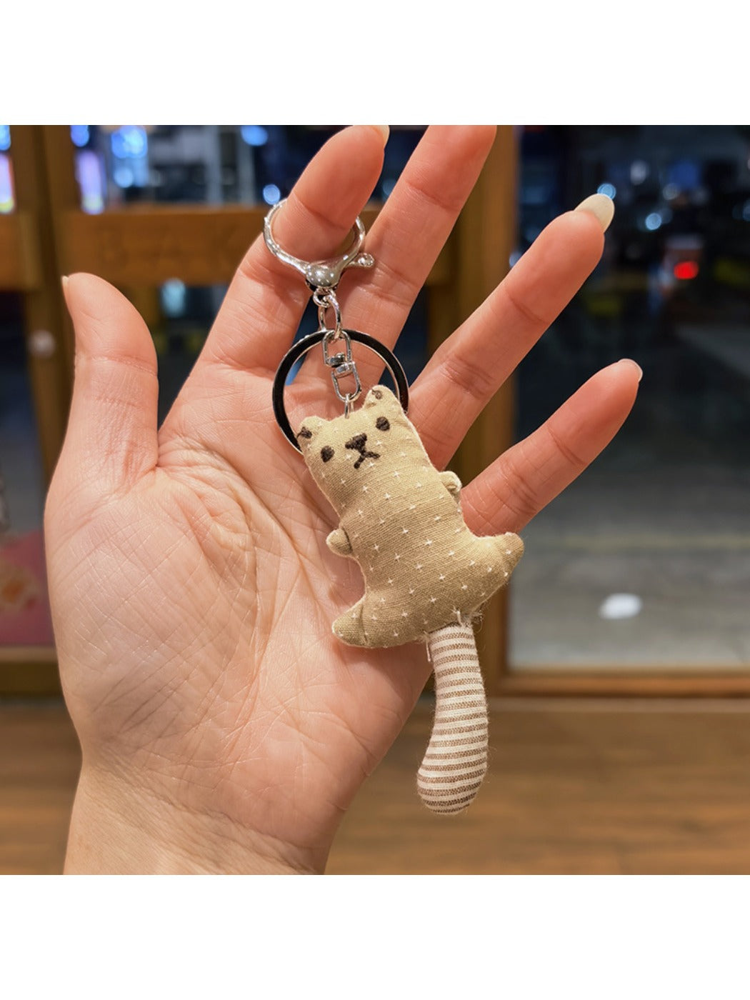 Bear keychain with a smiling expression and long tail curled around