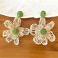 Earedge raffia flower earrings placed next to green leaves for natural aesthetic