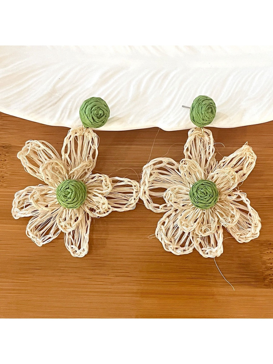 Earedge raffia flower earrings placed next to green leaves for natural aesthetic