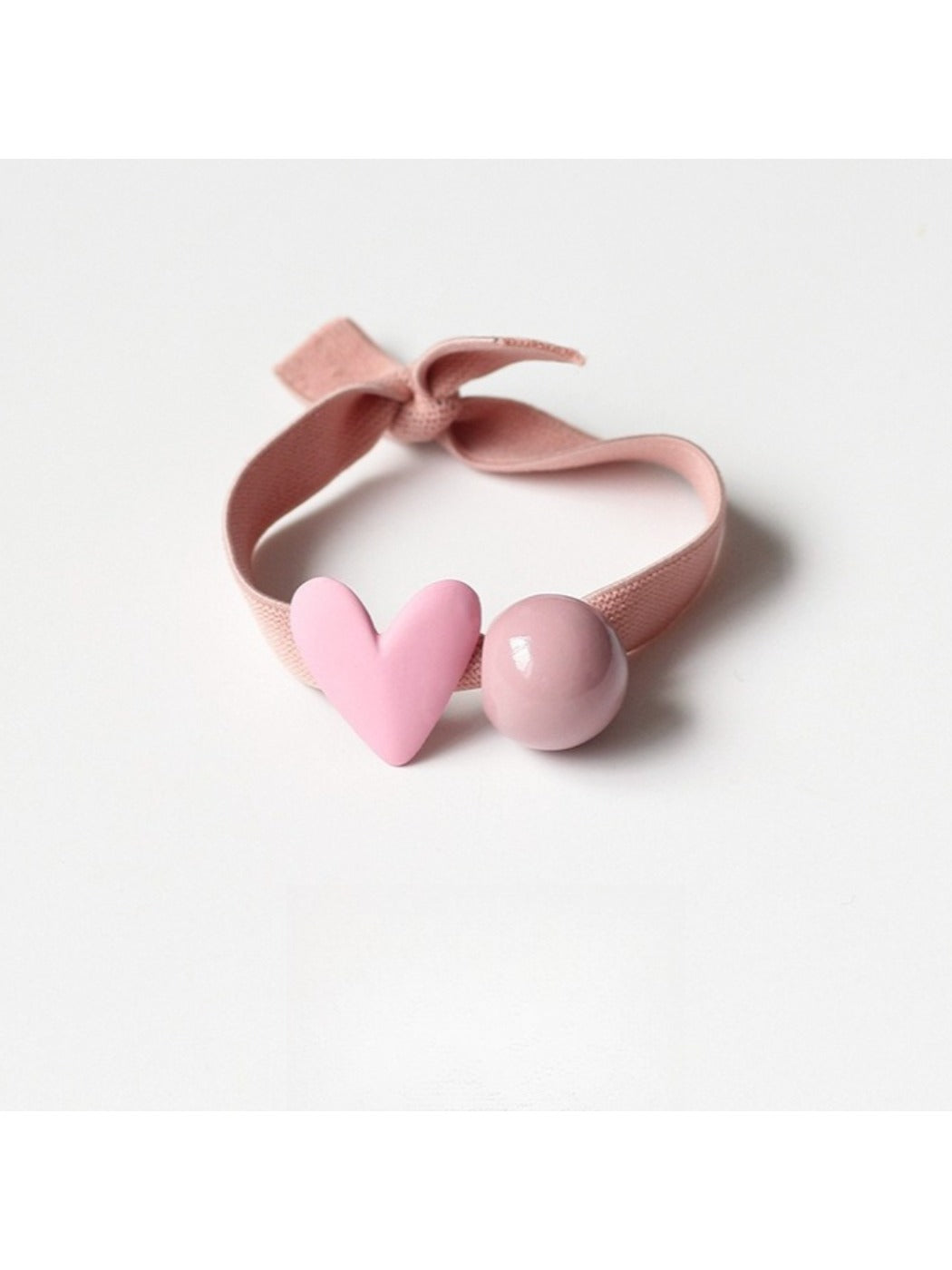 Red hair tie with a small white heart charm on a light fabric