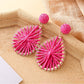 Earedge raffia earrings hanging on a decorative stand with soft lighting