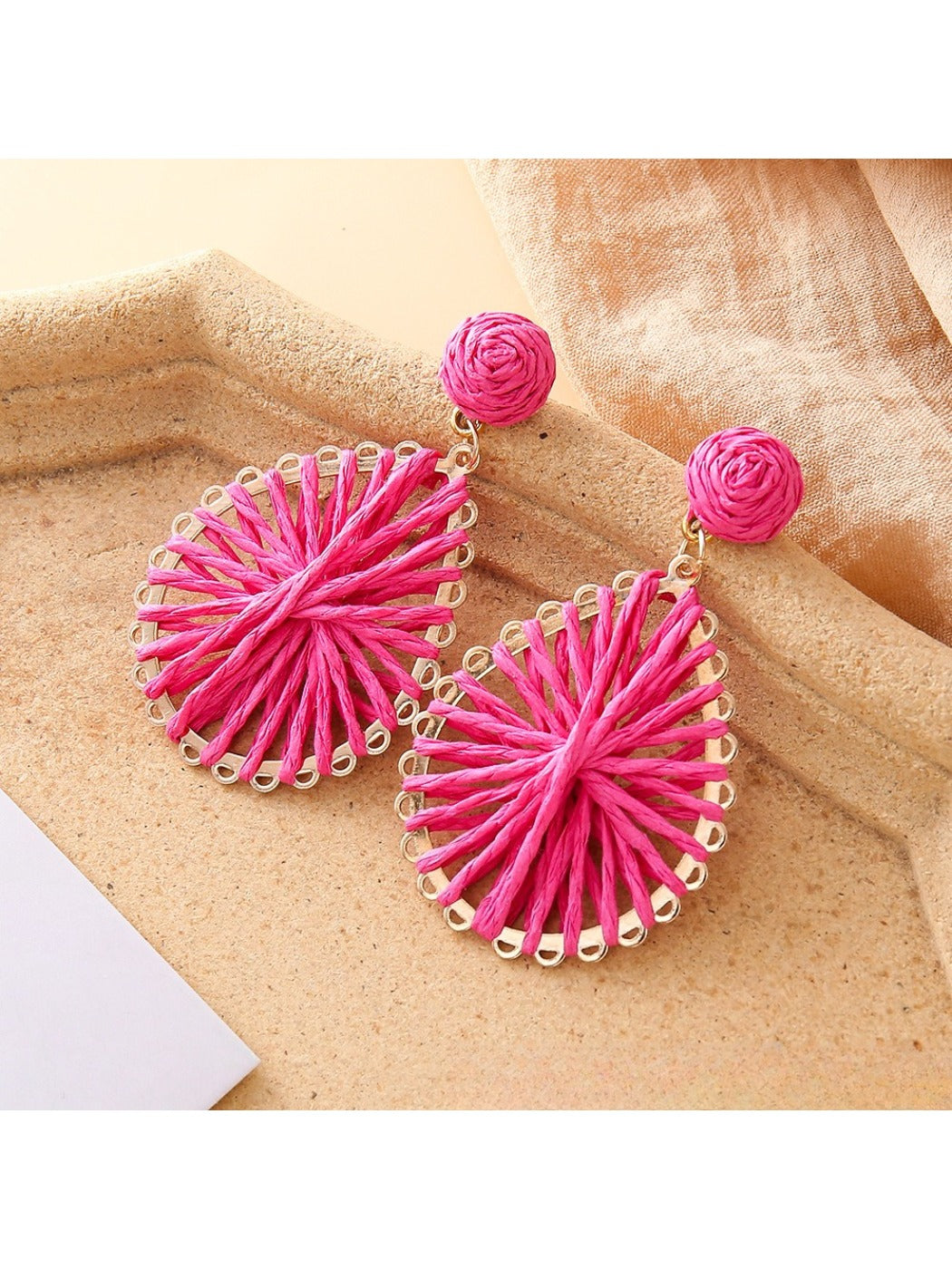 Earedge raffia earrings hanging on a decorative stand with soft lighting