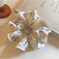 Close-up of Gifty satin scrunchie with pink and white floral print on a light background